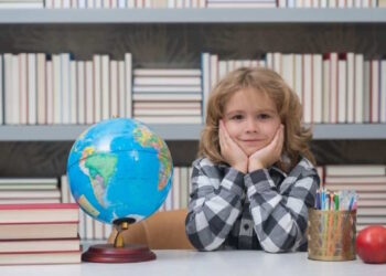 Школяр за столом із глобусом та книгами на тлі бібліотечних полиць - PedagogikaIN