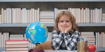 Школяр за столом із глобусом та книгами на тлі бібліотечних полиць - PedagogikaIN